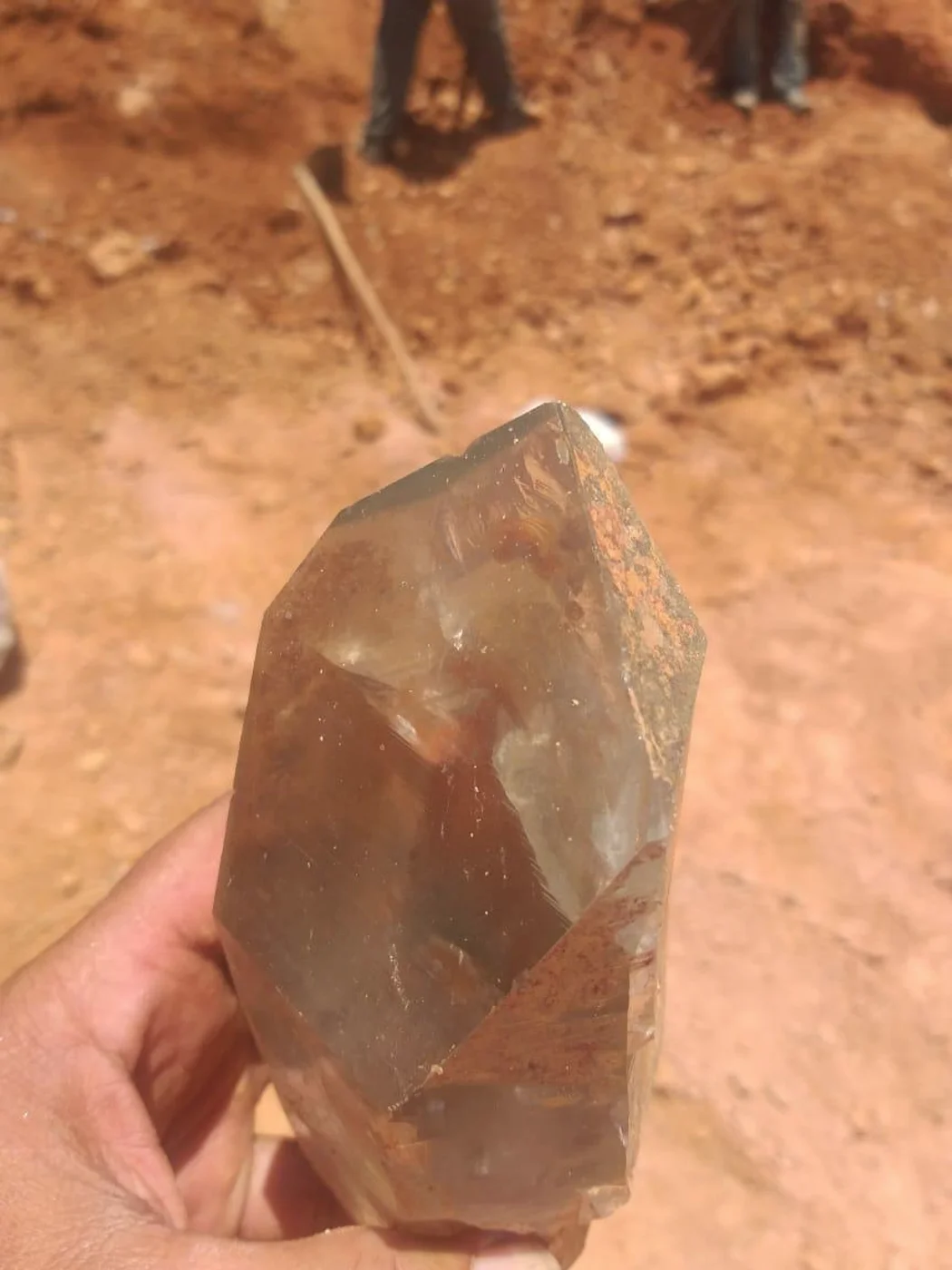 Trincheira aberta em Francisco Sá, terra revolvida e pessoas trabalhando ao fundo, com cristal fumê em primeiro plano.
